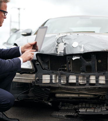 Male Insurance Loss Adjuster With Digital Tablet Inspecting Damage To Car From Motor Accident